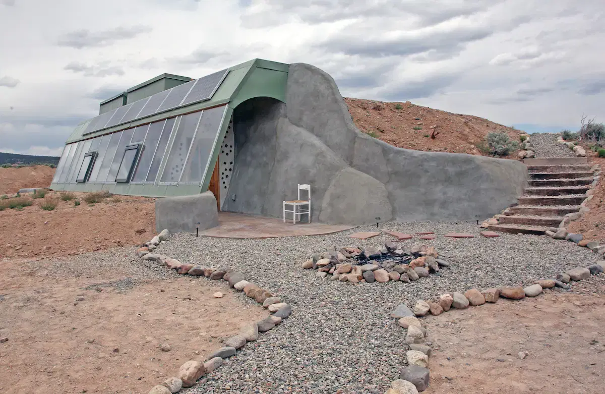 A modern house with solar panels is built partially into a hill.