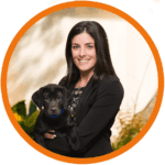 A woman in a black blazer is smiling while holding a black puppy.