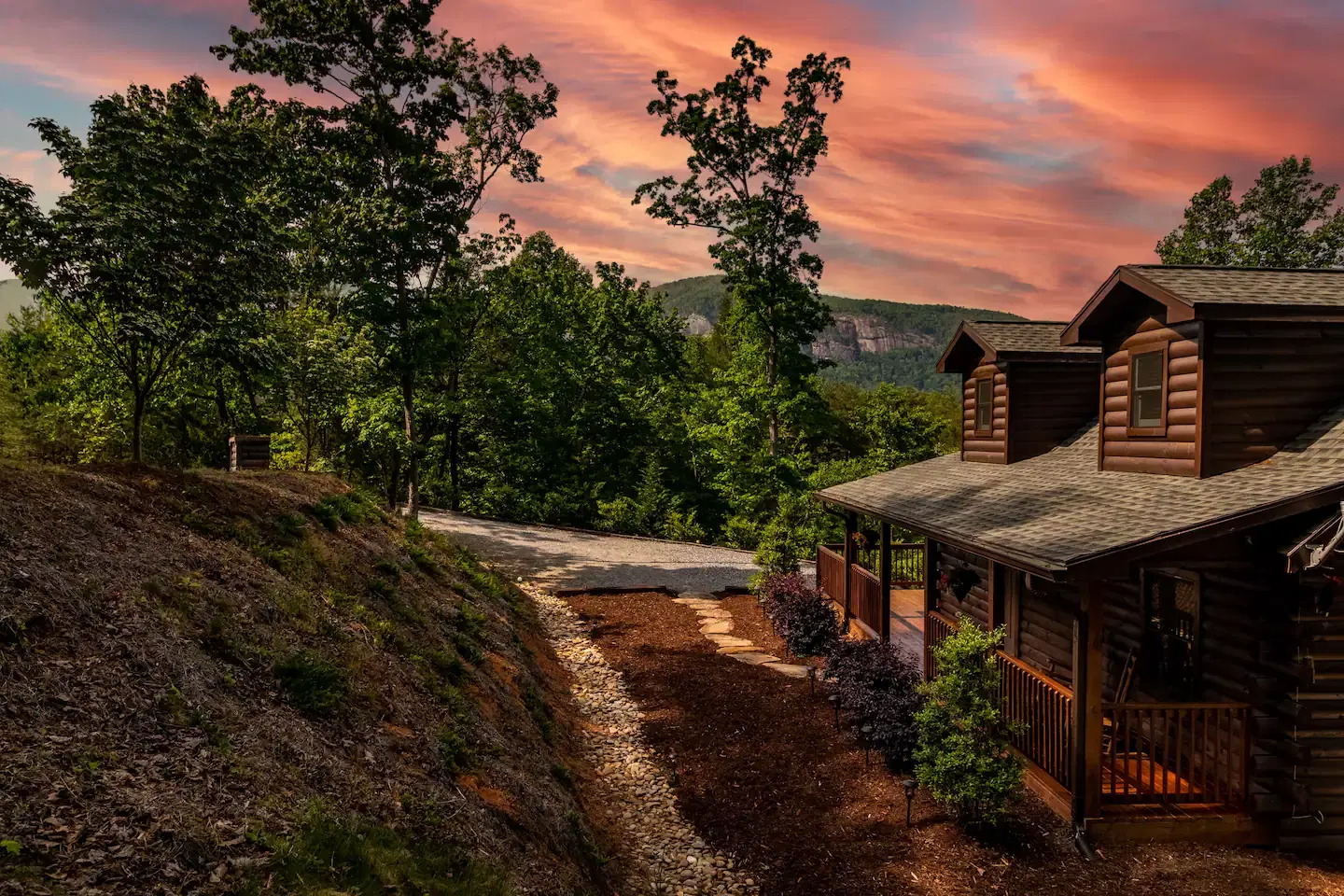 A log cabin with a porch is nestled among trees on a hill.