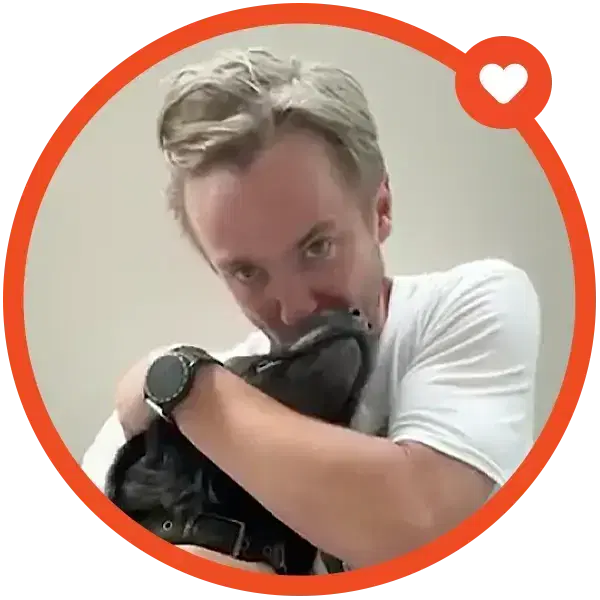 A person in a white shirt hugs a black dog partially covering their face inside an orange circle with a heart icon.